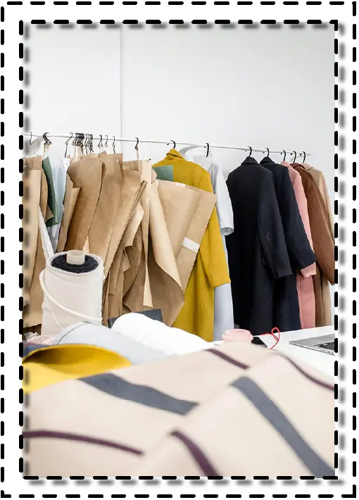 Taller de moda con moldes de papel, prendas colgadas y textiles sobre la mesa de trabajo