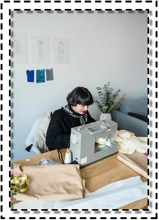 Diseñadora de moda concentrada en la máquina de coser, trabajando con telas claras en un entorno creativo y organizado.