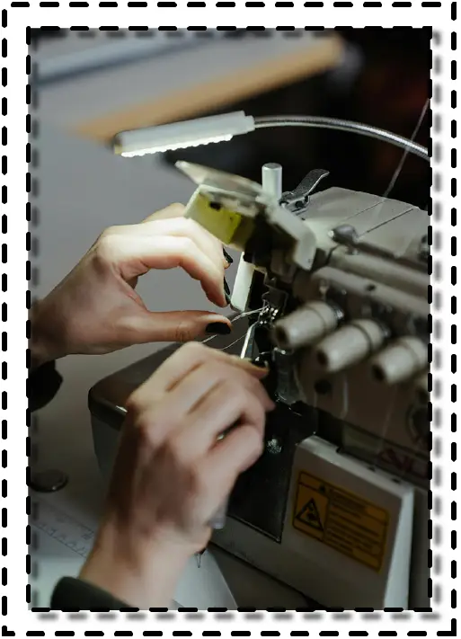 Manos operando una máquina overlock industrial en proceso de confección textil.