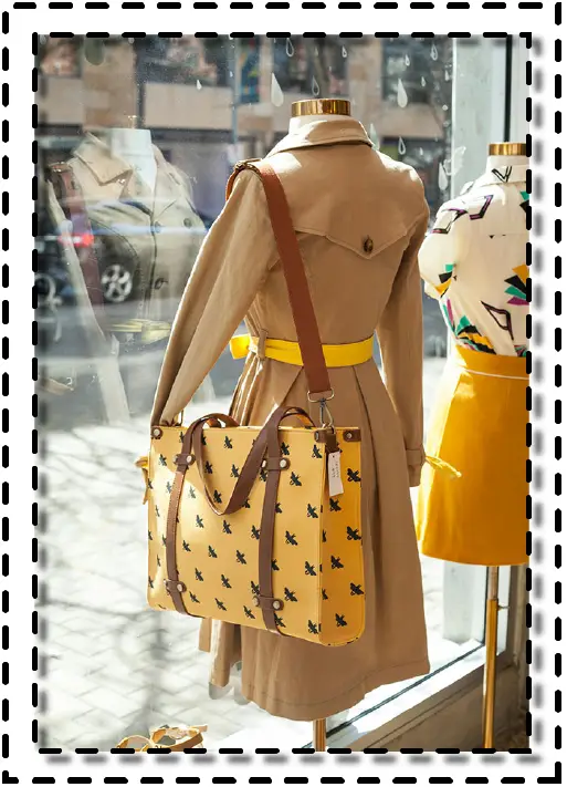 Vitrina de tienda con maniquíes vestidos en tonos beige y amarillo mostaza, acompañados de bolsos estampados.