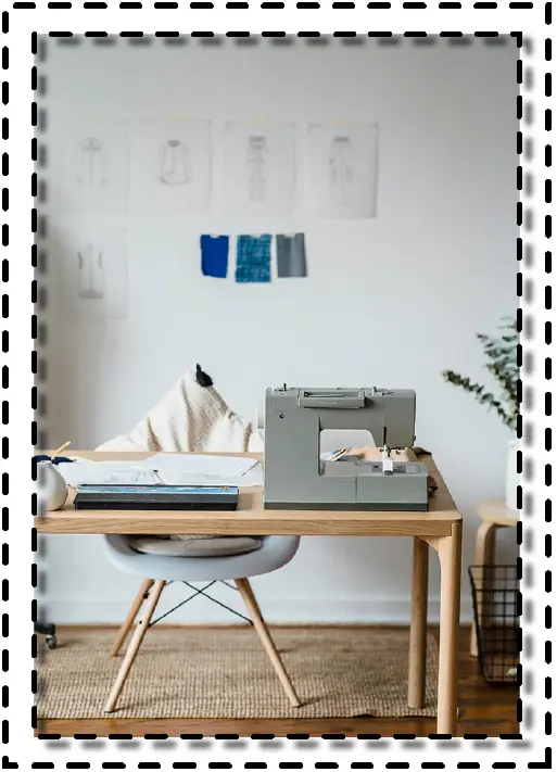 Estudio de diseño con máquina de coser sobre escritorio de madera, silla moderna y moldes técnicos colgados en la pared, representando un entorno de trabajo profesional.