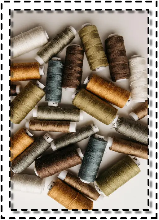 Hilos de coser en tonos tierra y neutros organizados sobre una superficie clara, representando variedad de insumos textiles en el mundo de la confección.