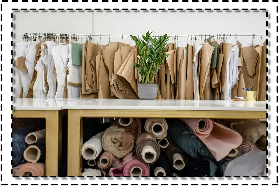 Estantería con patrones de papel colgados, telas enrolladas y una planta decorativa en un taller de diseño de moda.
