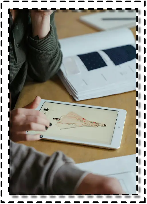 Personas revisando una ilustración de moda en una tablet, junto a muestras textiles y fichas técnicas, representando la integración del diseño digital en procesos creativos.