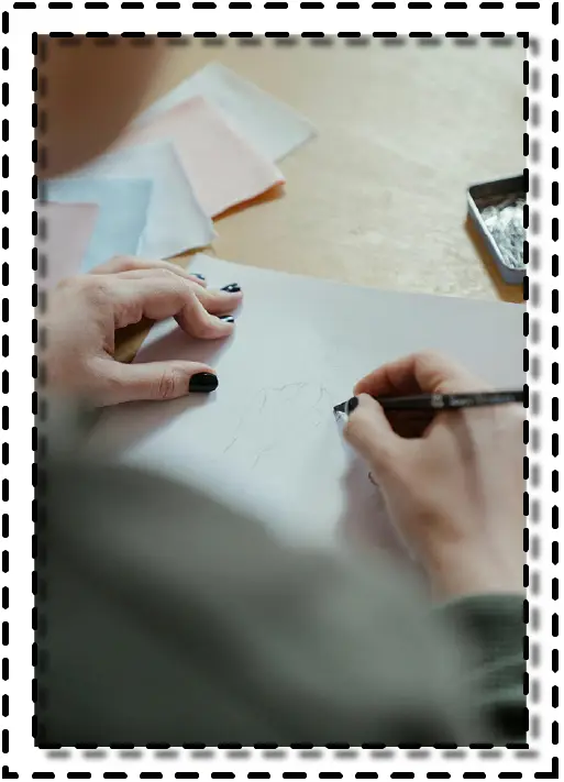 Persona dibujando a mano alzada un diseño de moda sobre papel, acompañada de muestras textiles.