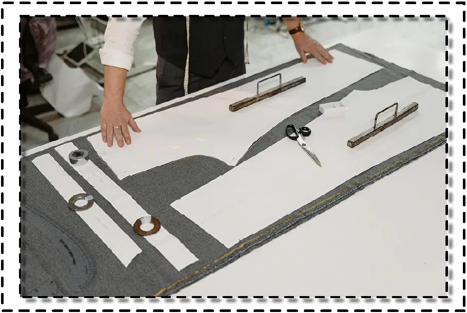 Patronista preparando el corte de tela sobre una mesa con moldes de papel, pesos, tijeras y herramientas de trazado.