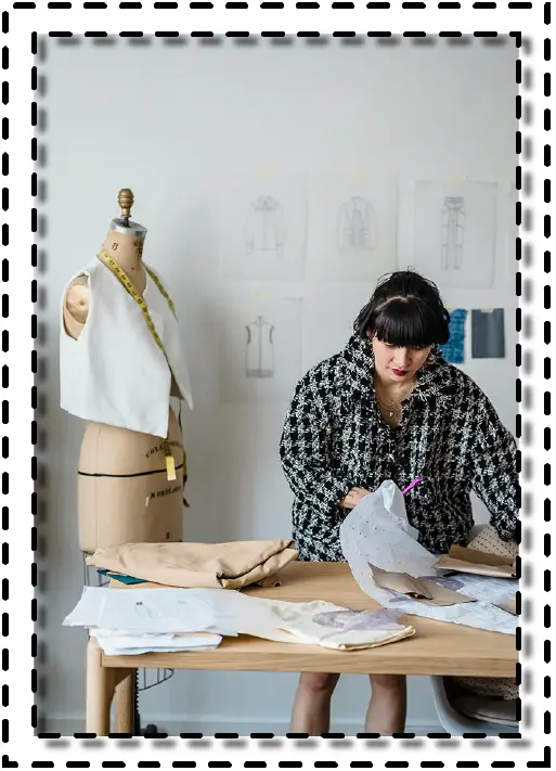 Diseñadora de moda trabajando con moldes de papel sobre una mesa, acompañada de un maniquí con prenda en proceso de confección.