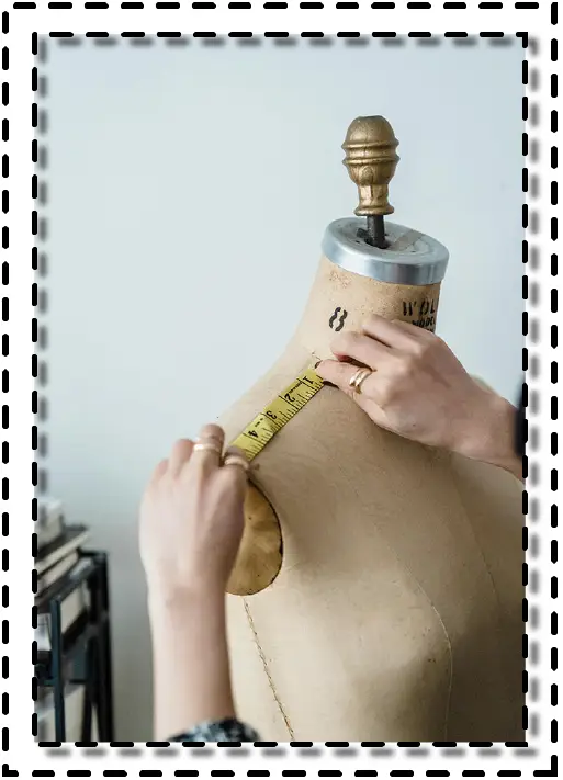 Manos midiendo el contorno del hombro sobre un maniquà de sastrerÃa con cinta métrica.