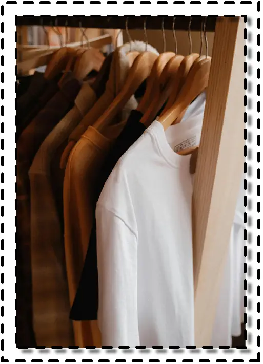 Camisetas colgadas en perchas de madera dentro de un armario abierto.