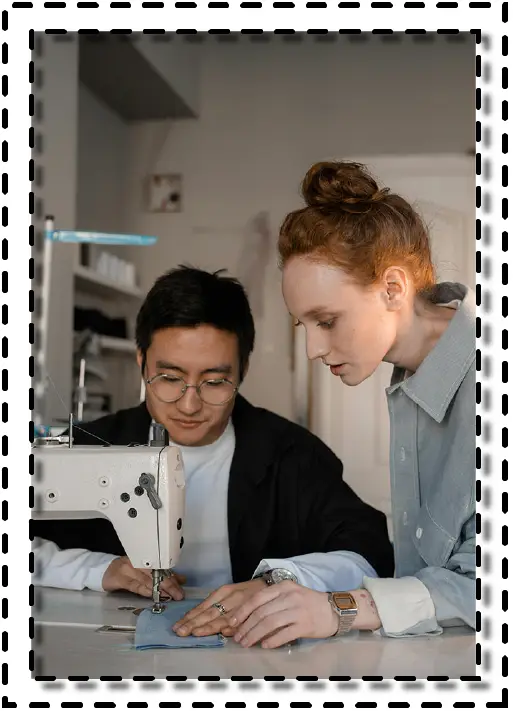 Dos personas trabajando en equipo frente a una máquina de coser industrial, concentradas en una costura precisa.