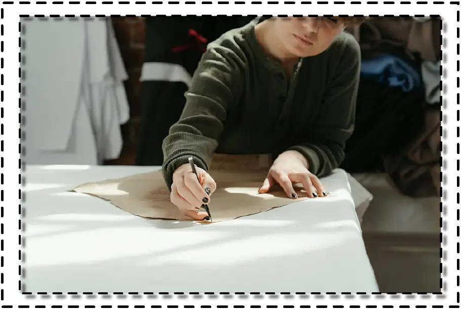 Persona trazando un molde de prenda sobre papel kraft en una mesa de trabajo, con luz natural y telas al fondo.