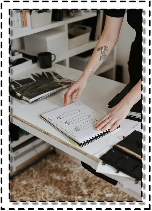 Persona hojeando un cuaderno con moldes técnicos de prendas en un espacio de trabajo con materiales de costura.