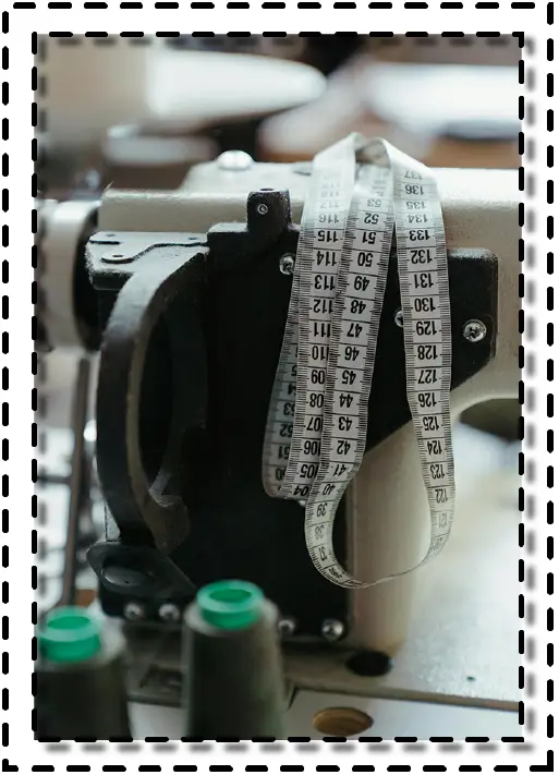 Máquina de coser industrial con una cinta métrica colgando, en un ambiente de taller de costura.