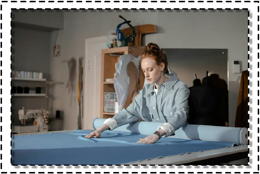 Diseñadora extendiendo tela sobre mesa de corte en taller de confección.